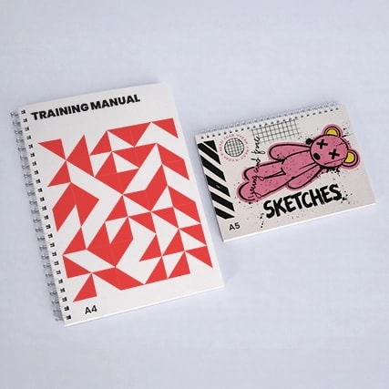 Two spiral-bound notebooks labeled "Training Manual" (A4) and "Sketches" (A5) on a white surface.