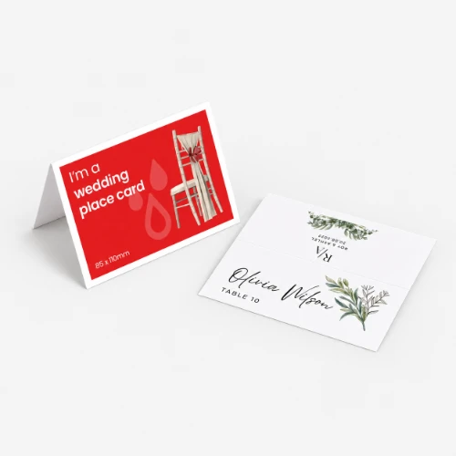 Two folded wedding place cards: one red with a chair graphic, one white with floral details.