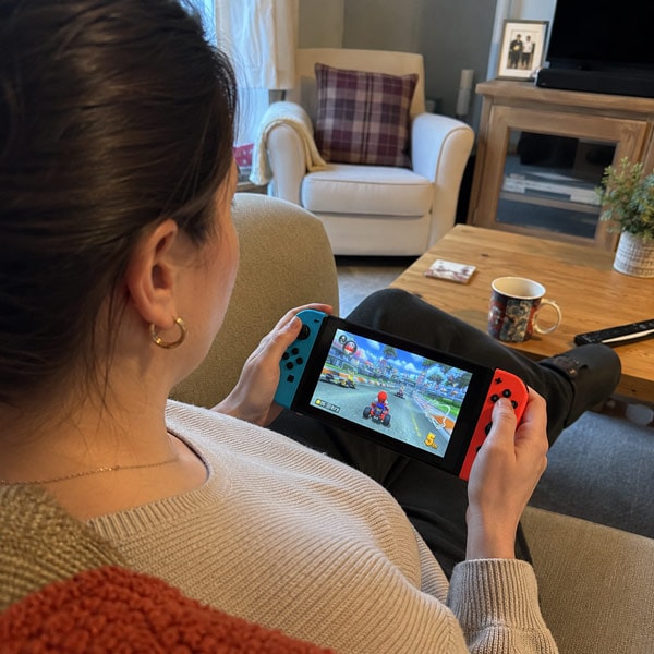 Person playing Mario Kart on a Nintendo Switch while sitting on a couch in a living room.