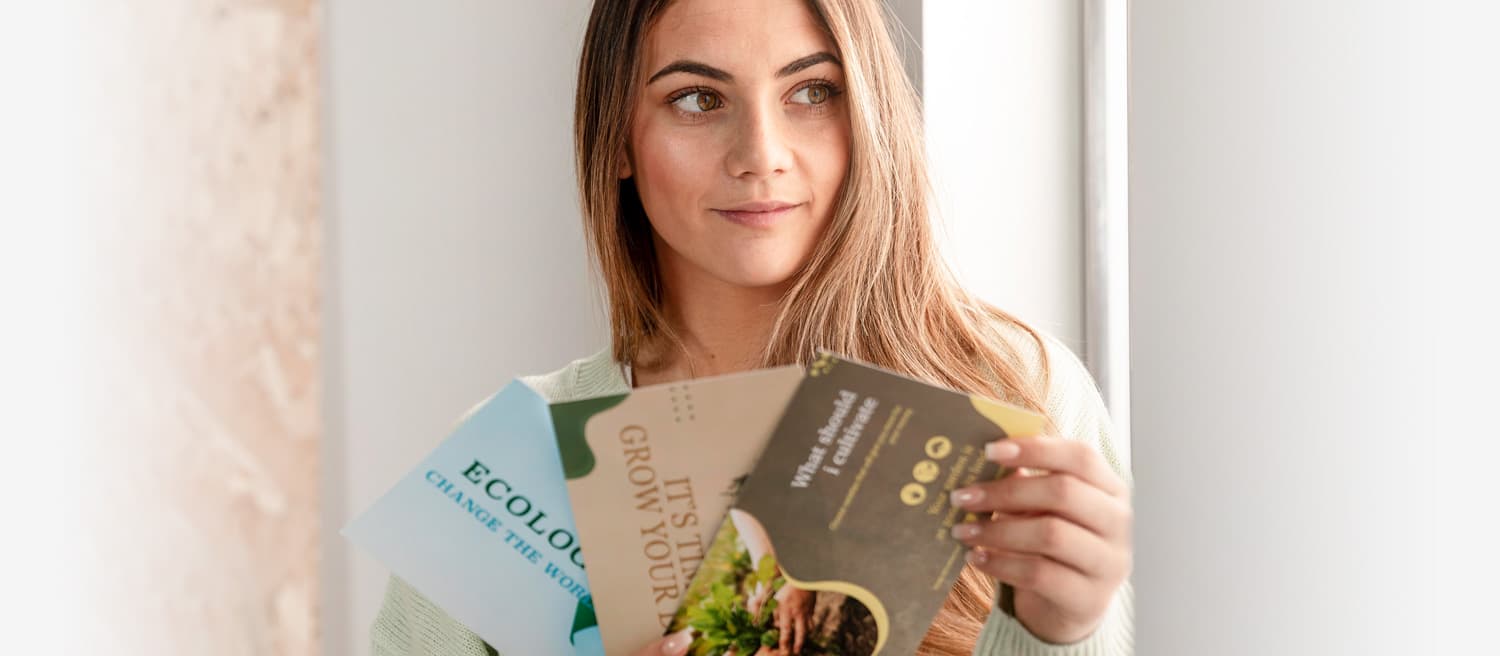 A woman displays three distinct flyers, showcasing various designs and information in her hands.
