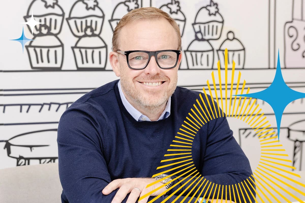 Man with glasses smiling at a table, illustrated cupcake background and yellow graphic overlay.