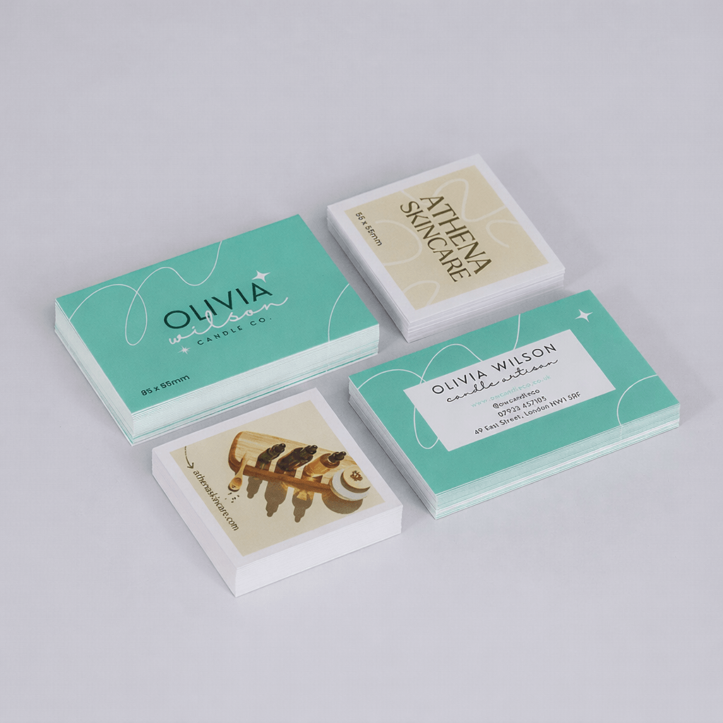 Four stacks of laminated business cards with different designs are arranged on a light gray surface.