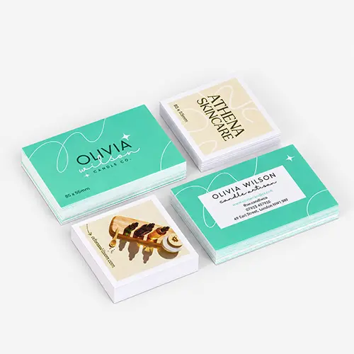 Four stacks of laminated business cards with different designs are arranged on a light gray surface.