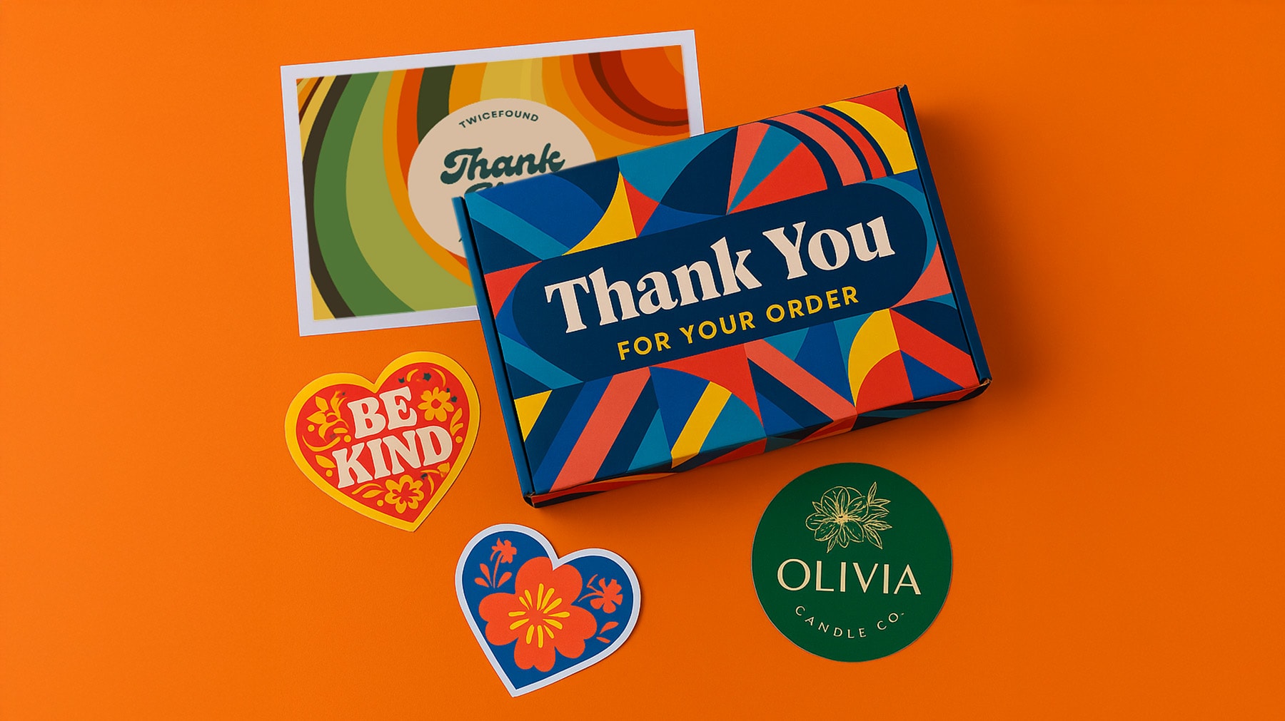 Colourful thank you box, stickers, and postcard on orange background.