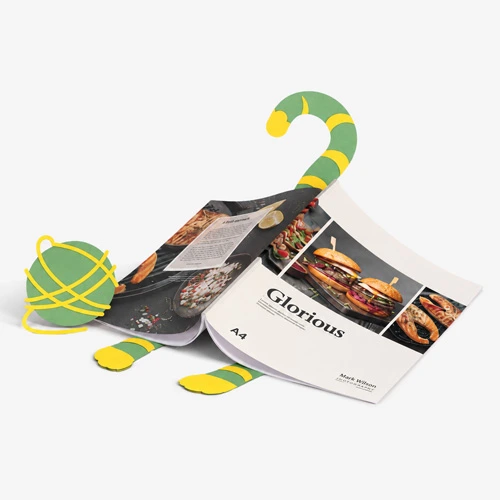 A magazine is propped open by a flat, cartoon-like lizard cutout on a light gray background.