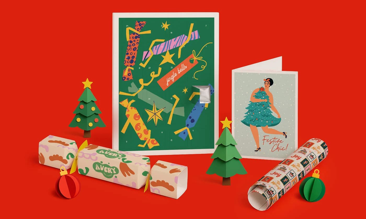 Two festive greeting cards, paper trees, crackers, and wrapping paper on a red background.
