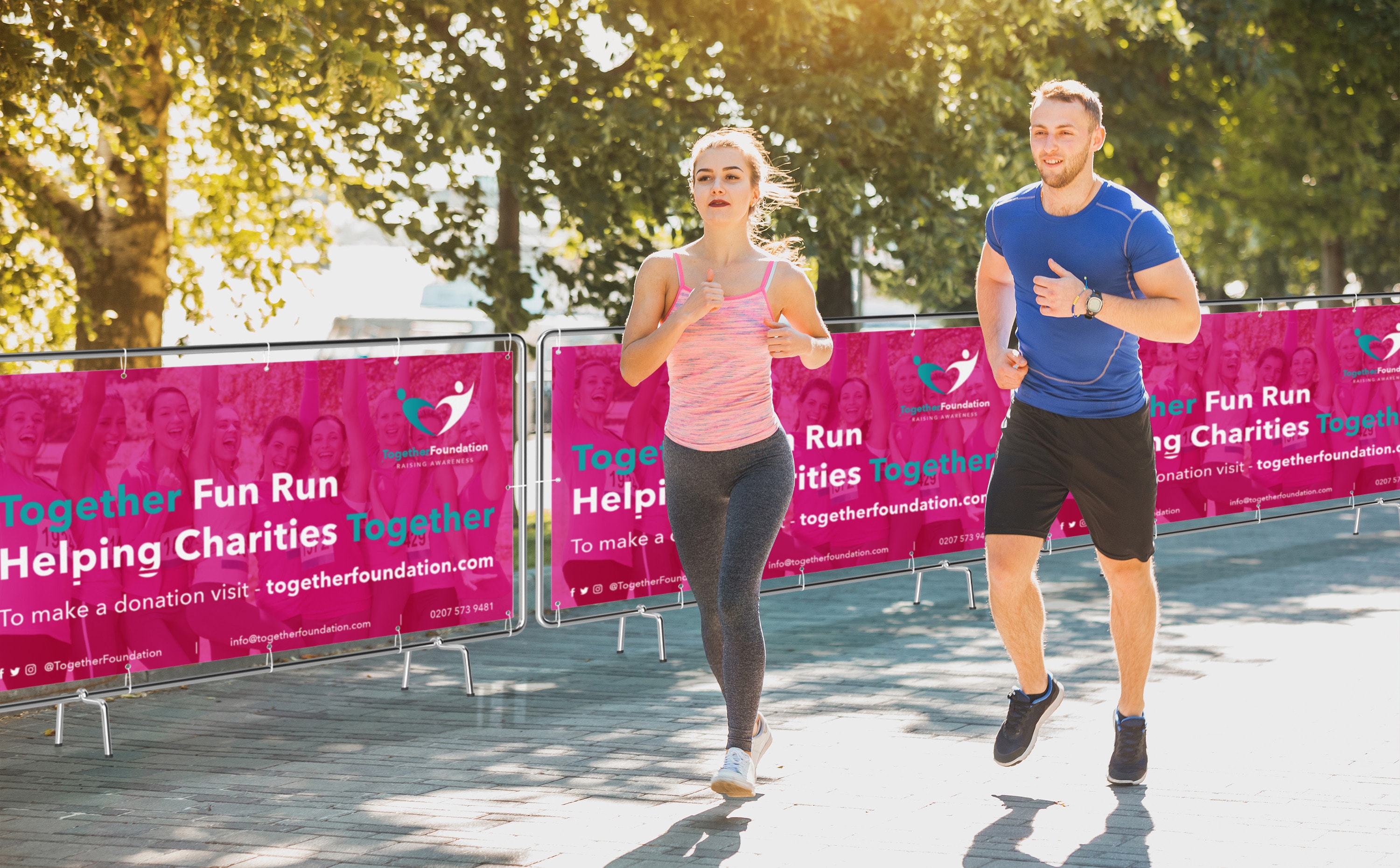 Two people jogging at a charity fun run event, with charity banners in the background.