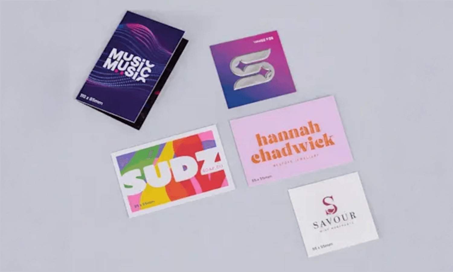 Five colourful business cards with various designs arranged on a wide, light grey background.
