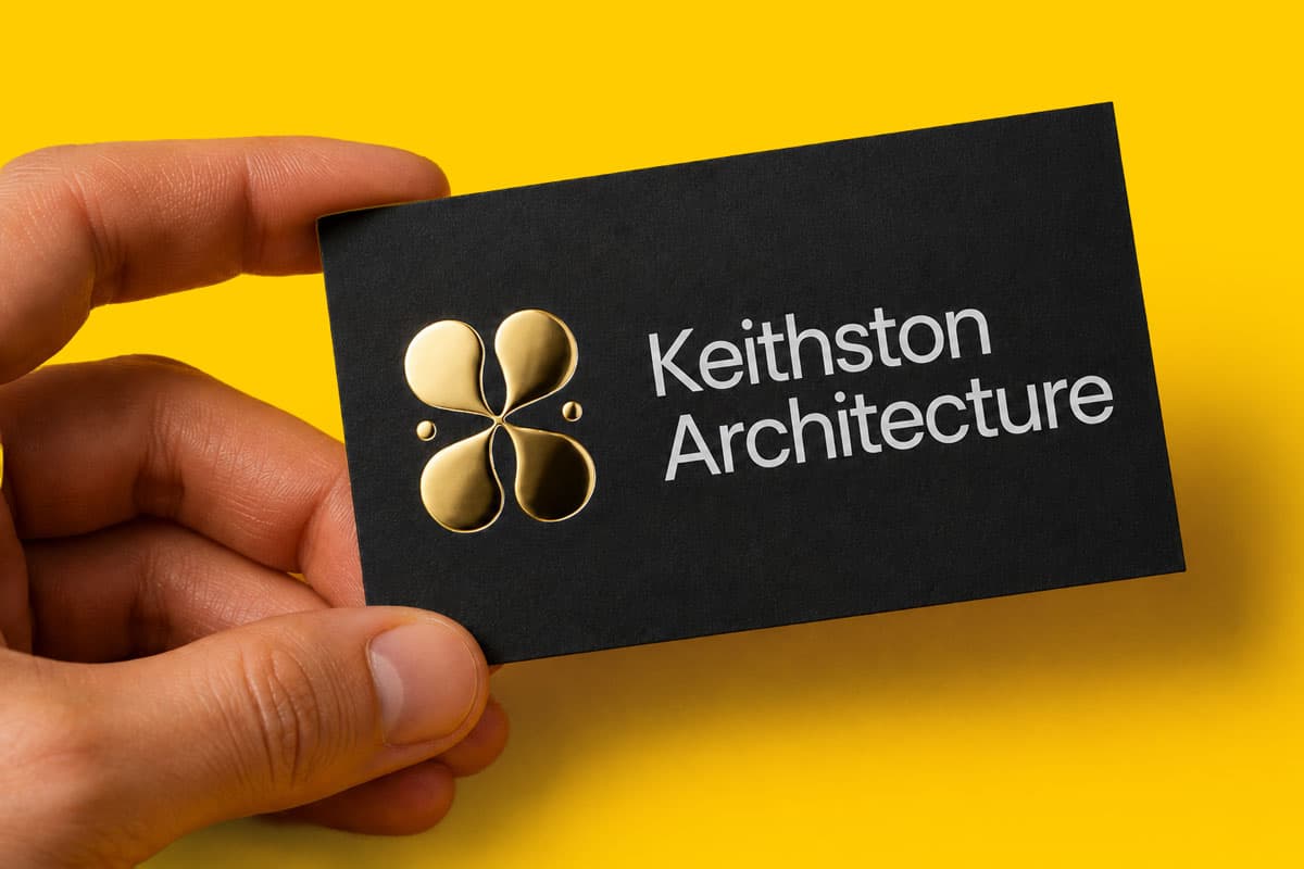 Hand holding a black business card with "Keithston Architecture" and a gold logo on it.