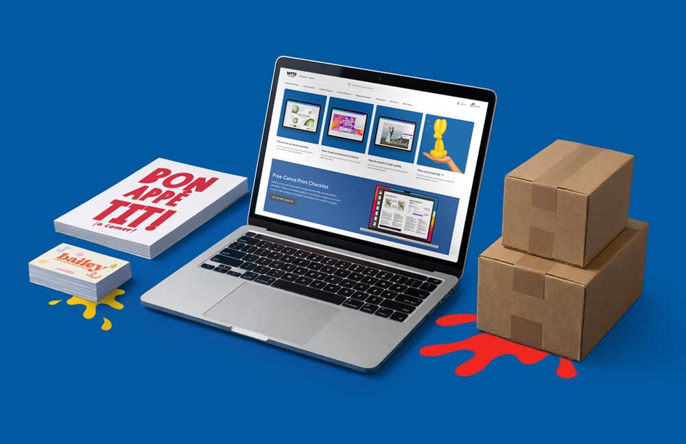 A laptop, two boxes, a notebook, and Canva business cards on a blue background.