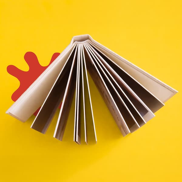 Open book with fanned pages on a yellow background with a red abstract shape behind it.