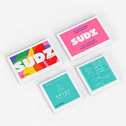 Four colourful rectangular recycled business cards with bold, modern designs on a light gray background.