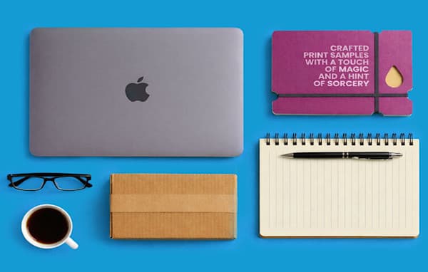Laptop, notebook with pen, glasses, coffee, box, and business card on a blue setting.