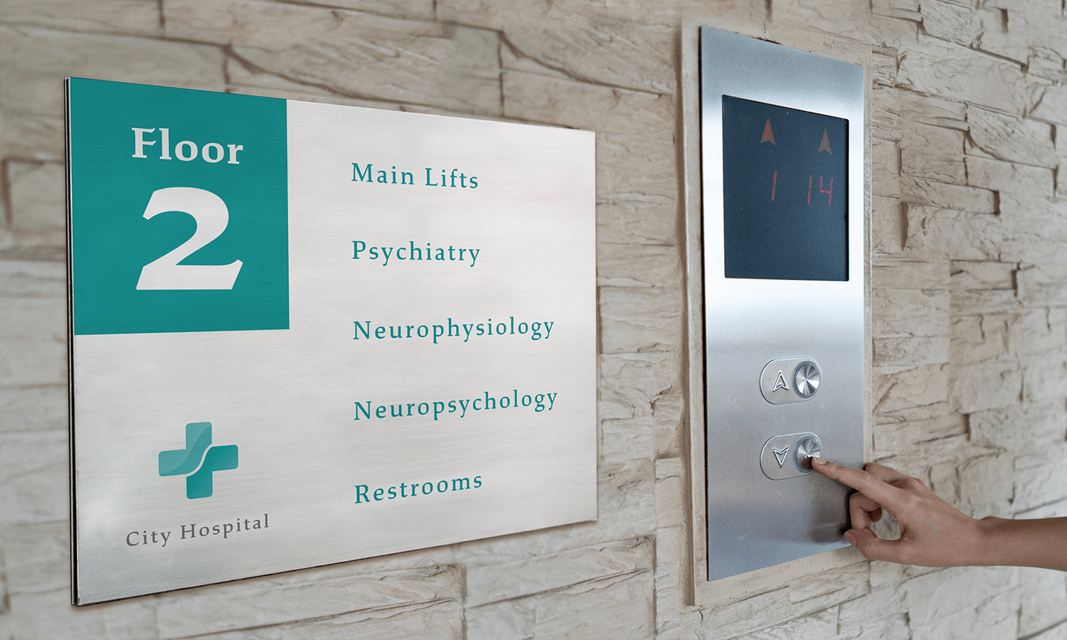 A person presses an elevator button near a dibond hospital sign listing departments on floor 2.