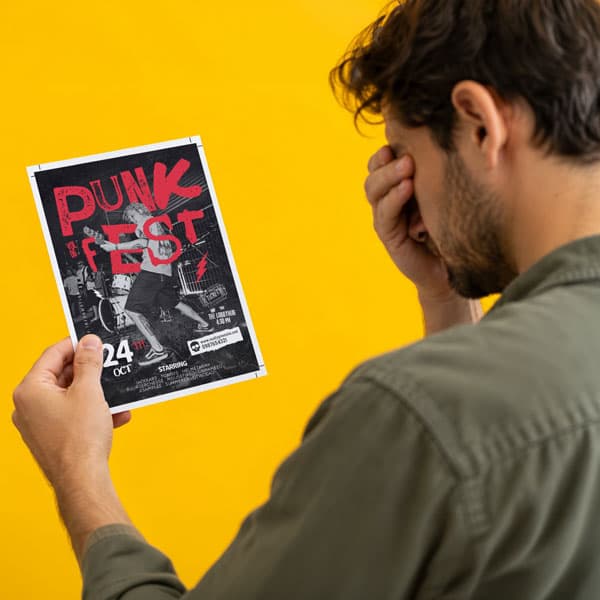 Man holds a punk festival flyer, covering his face with his hand against a yellow background.