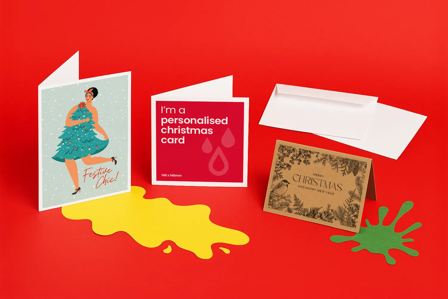 Three different Christmas cards and two envelopes are displayed on a red background with paint splashes.
