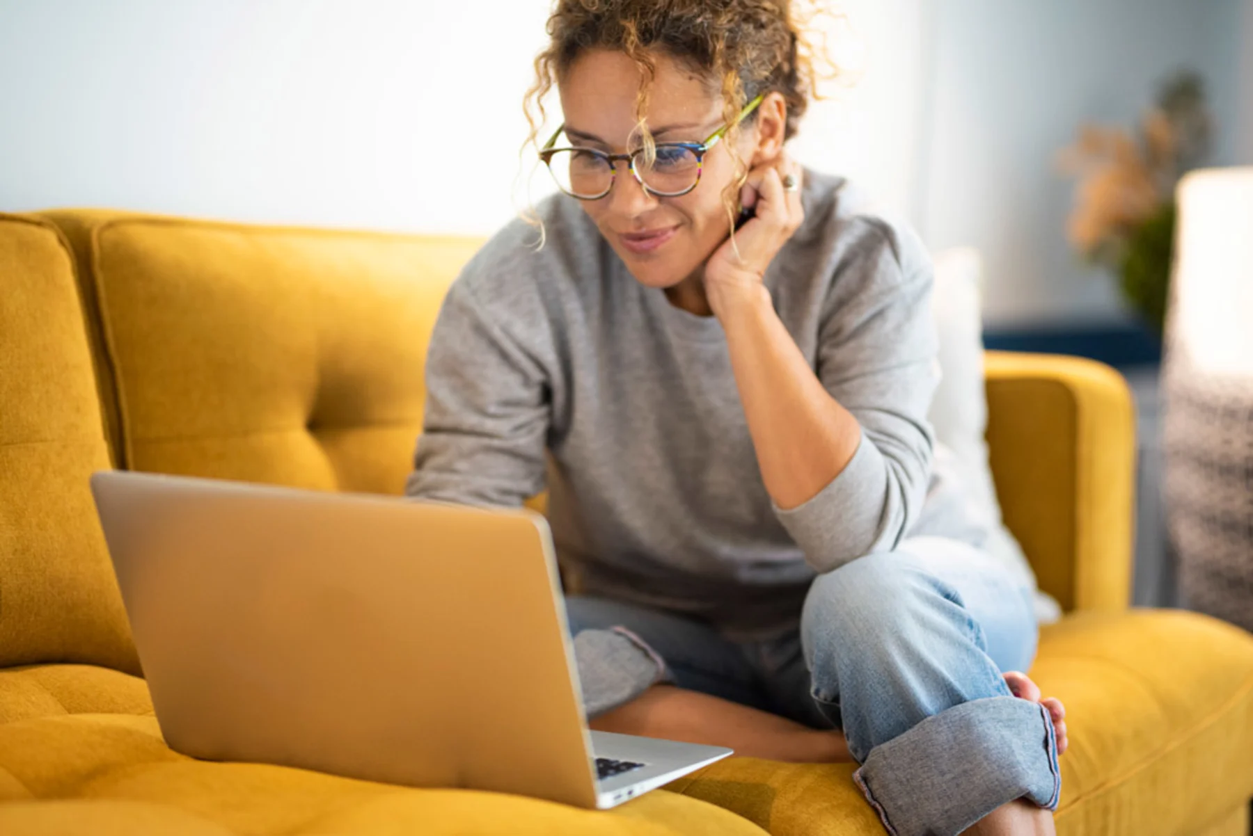 A woman comfortably sitting on a couch, engaged with her laptop
