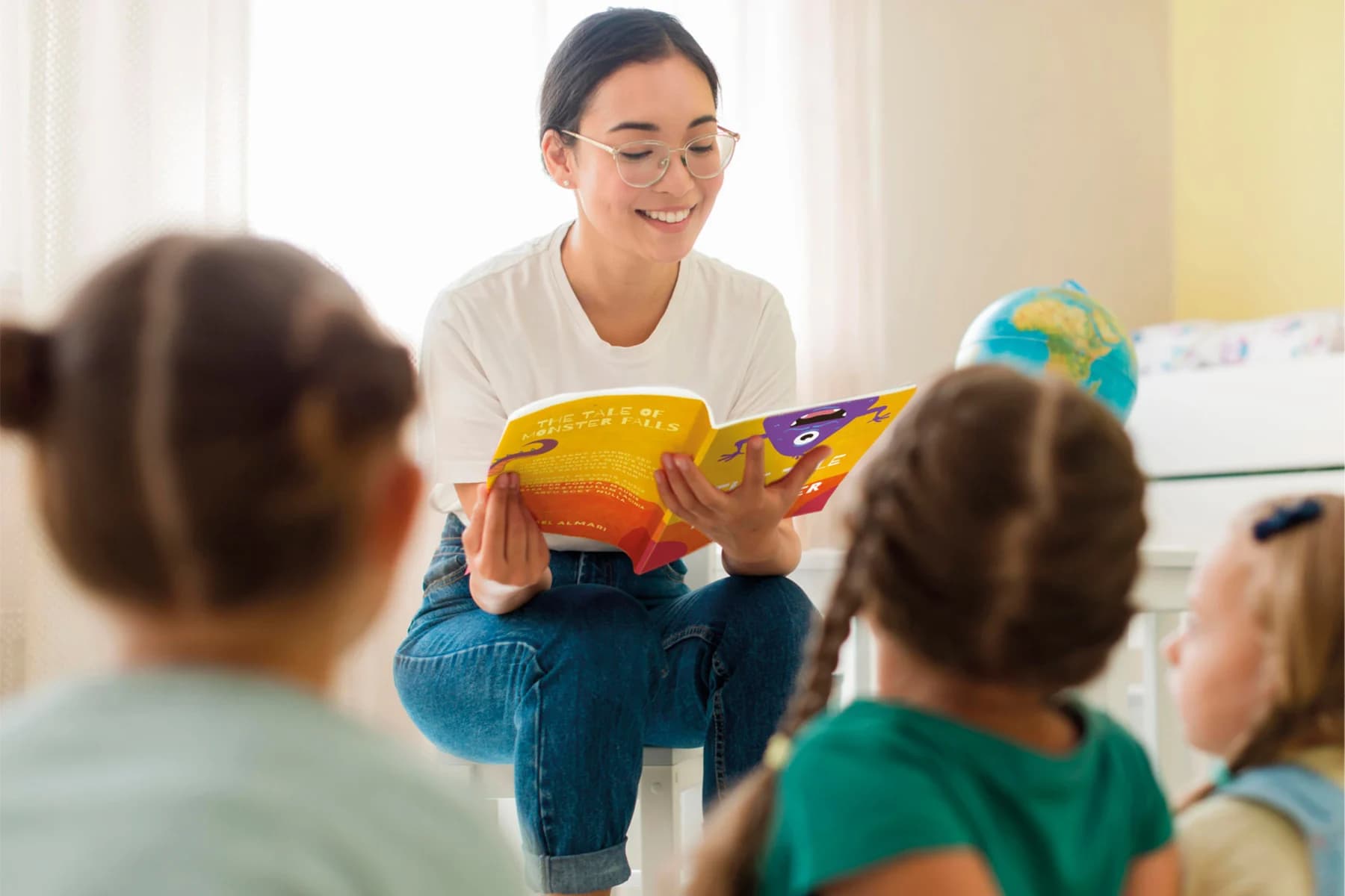 A woman engagingly reads a story to a group of attentive children in a bright classroom setting