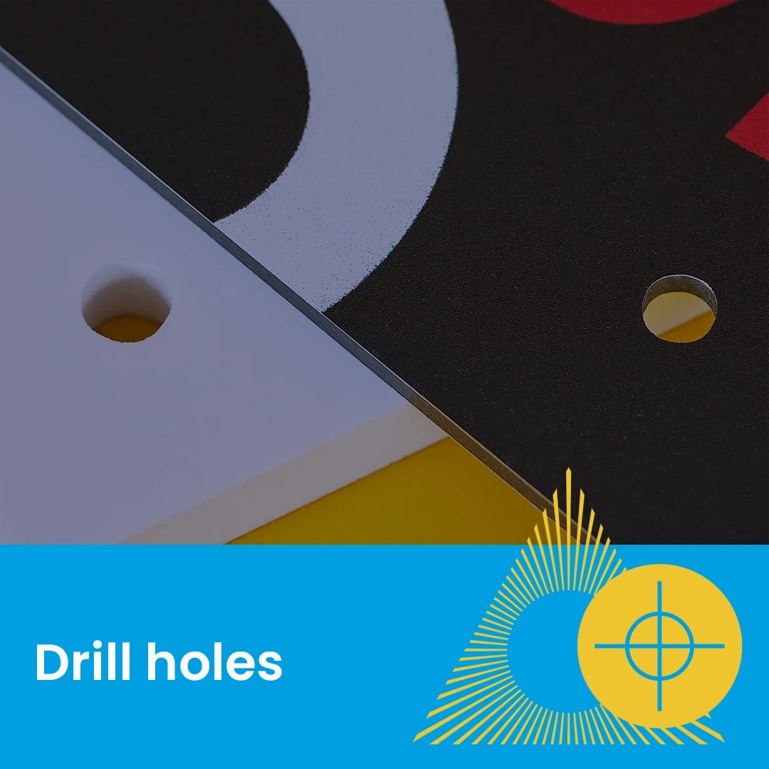 Close-up of two boards with round drill holes, one white and one black, above a blue label.