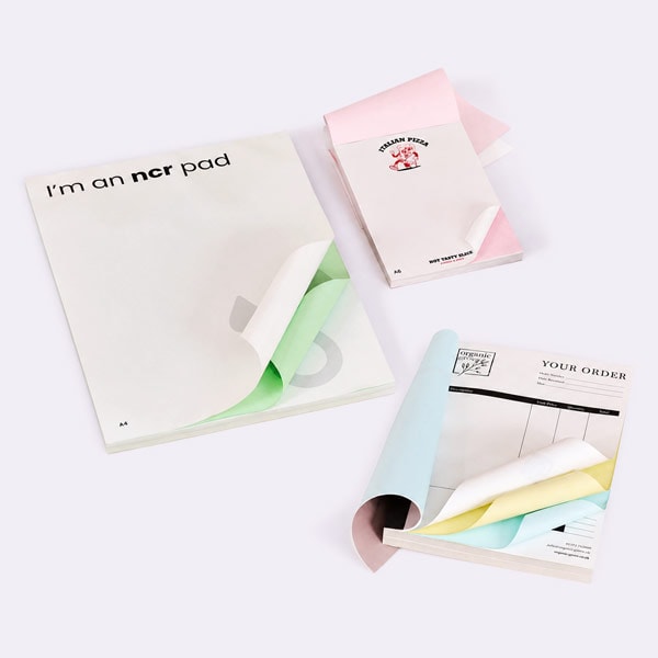 Three NCR pads with colored carbonless pages shown partially open on a white background.