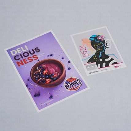 Two printed bus shelter posters on a flat surface, one with food and one with abstract art and event details.