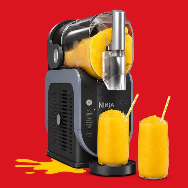 Ninja appliance making orange slush with two filled glasses and a spill on a red background.