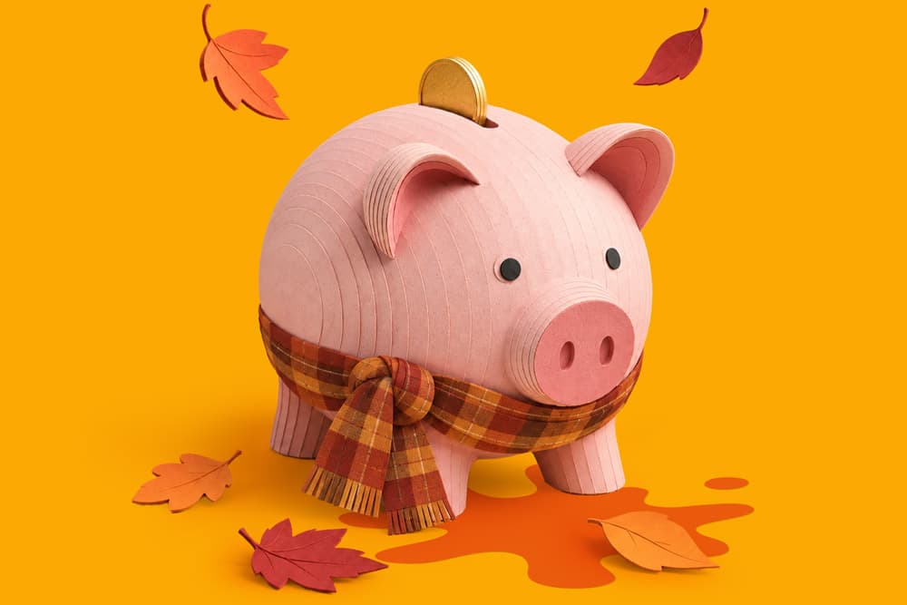 A piggy bank wearing a plaid scarf with autumn leaves on a yellow background.