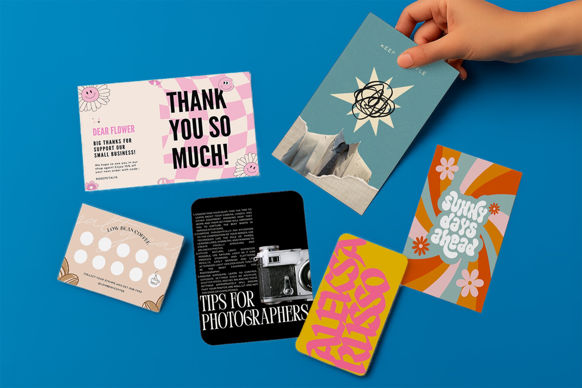 A hand arranges six colorful postcards and cards on a blue surface.