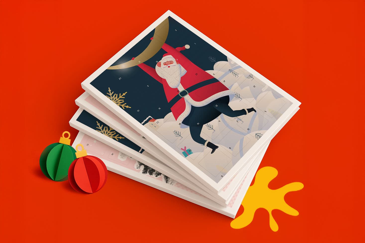 Stack of illustrated holiday cards featuring Santa, next to two paper ornaments on a red surface.