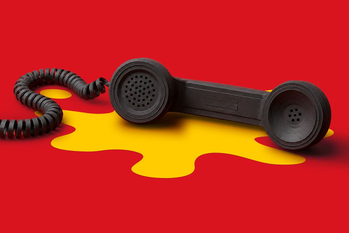 Black telephone receiver on a red surface with a yellow irregular shape beneath it.