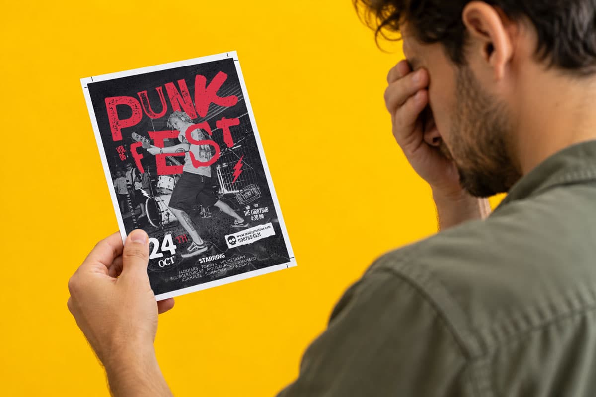 Man holding a “Punk Fest” flyer against a yellow background, covering his face with his hand.
