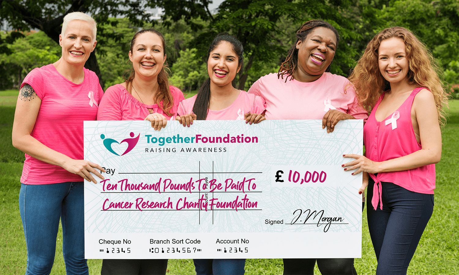 Five women in pink hold a large £10,000 branded charity donation giant cheque for cancer research.