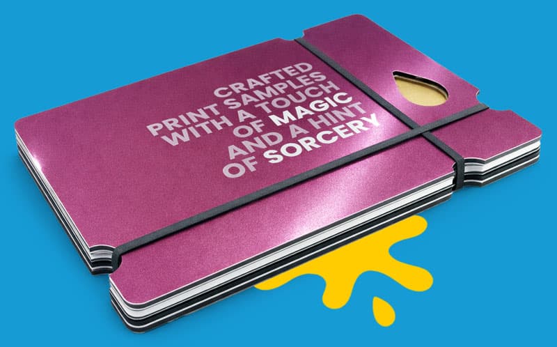 Stack of metallic print samples, held by black bands on a blue background with yellow paint.