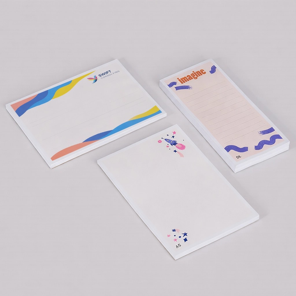 Three decorated notepads with different designs and lined or blank pages on a plain background.