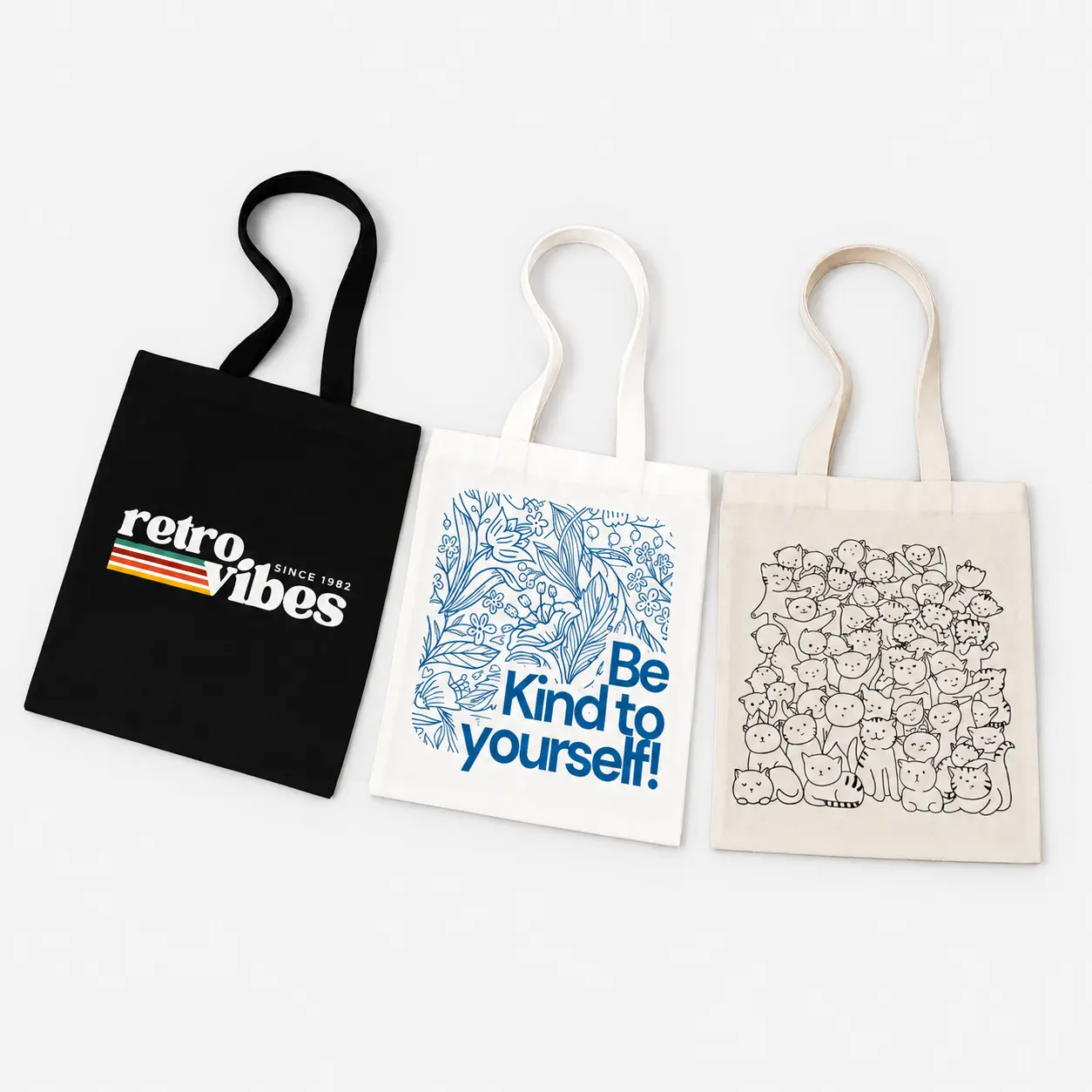 Three tote bags featuring prints: “retro vibes,” “Be Kind to yourself,” and a crowd of cats.