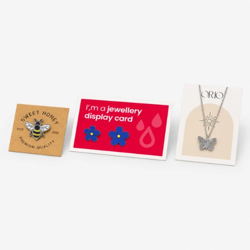 Three pieces of jewelry on display cards: a bee pin, blue flower earrings, and a butterfly necklace.