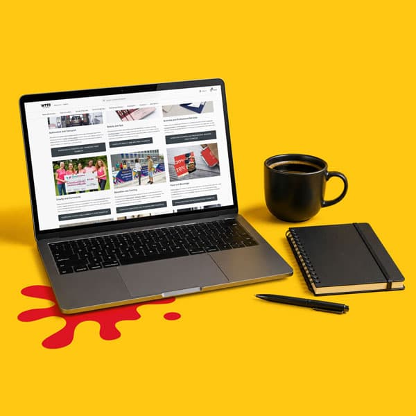 Laptop, notebook, pen, and coffee cup on yellow desk with a red splash under the laptop.