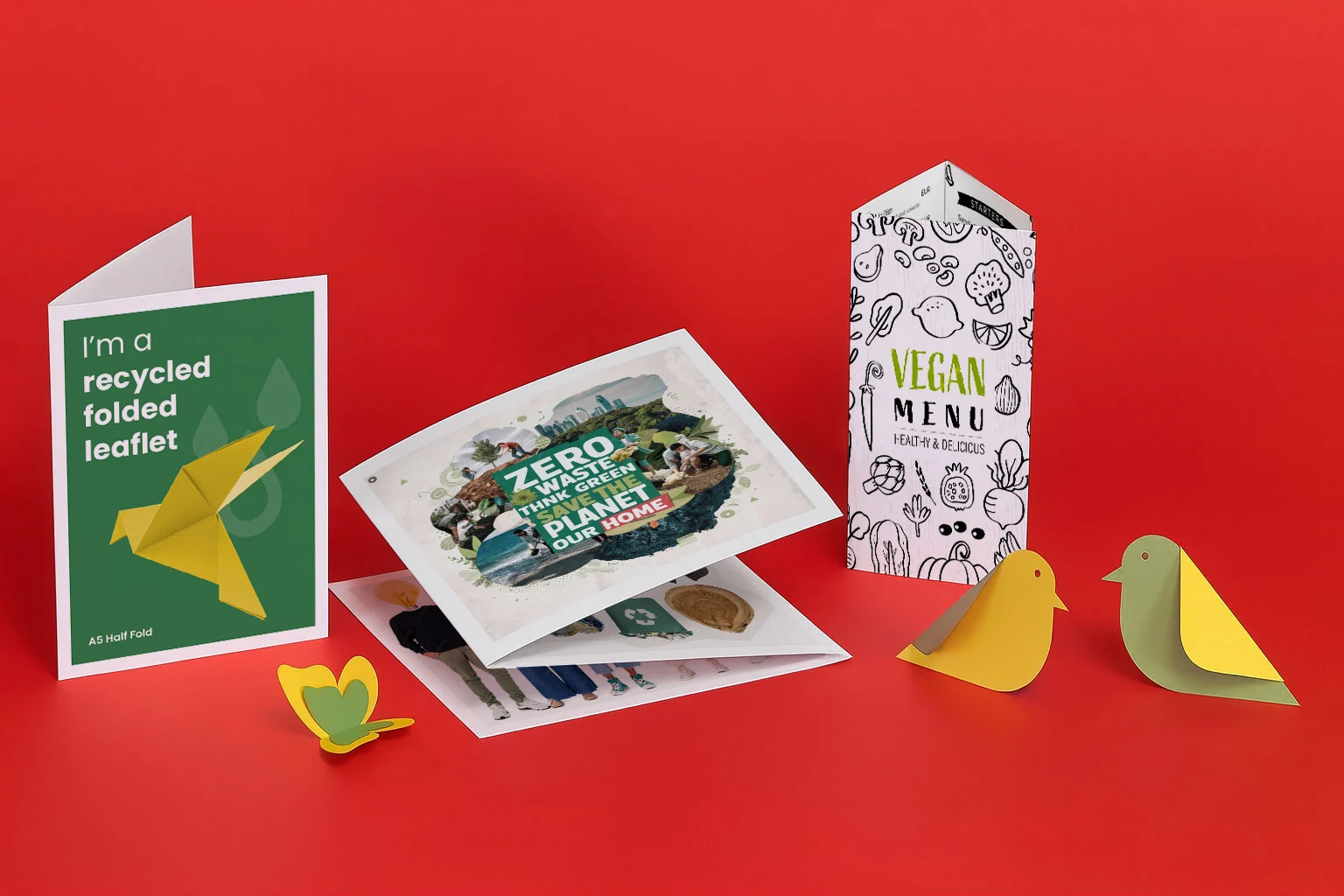 Various eco-friendly printed paper products displayed on a red surface, including menus and leaflets.