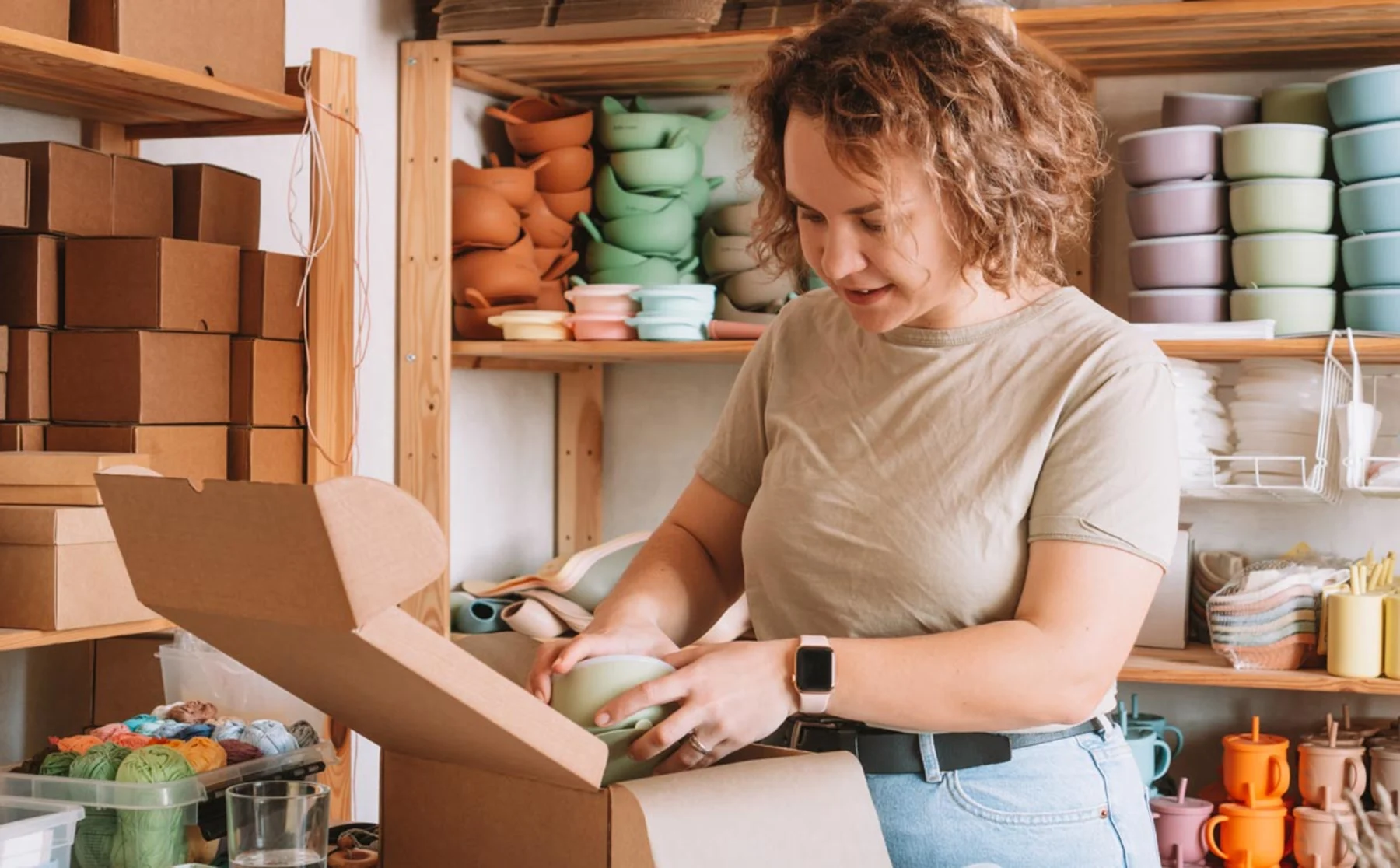 A woman carefully packs various items into a cardboard box