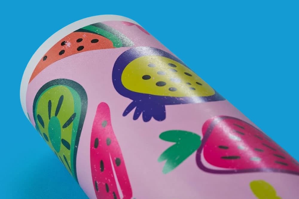 A rolled paper with colorful fruit illustrations on a pink background, placed on blue surface.