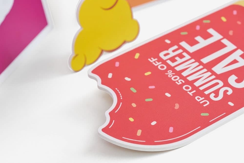 Red popsicle-shaped summer sale sign with a bite mark and colourful sprinkles on white background.