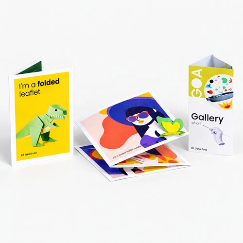 Three colourful folded leaflets and cards are displayed standing and lying on a gray surface.
