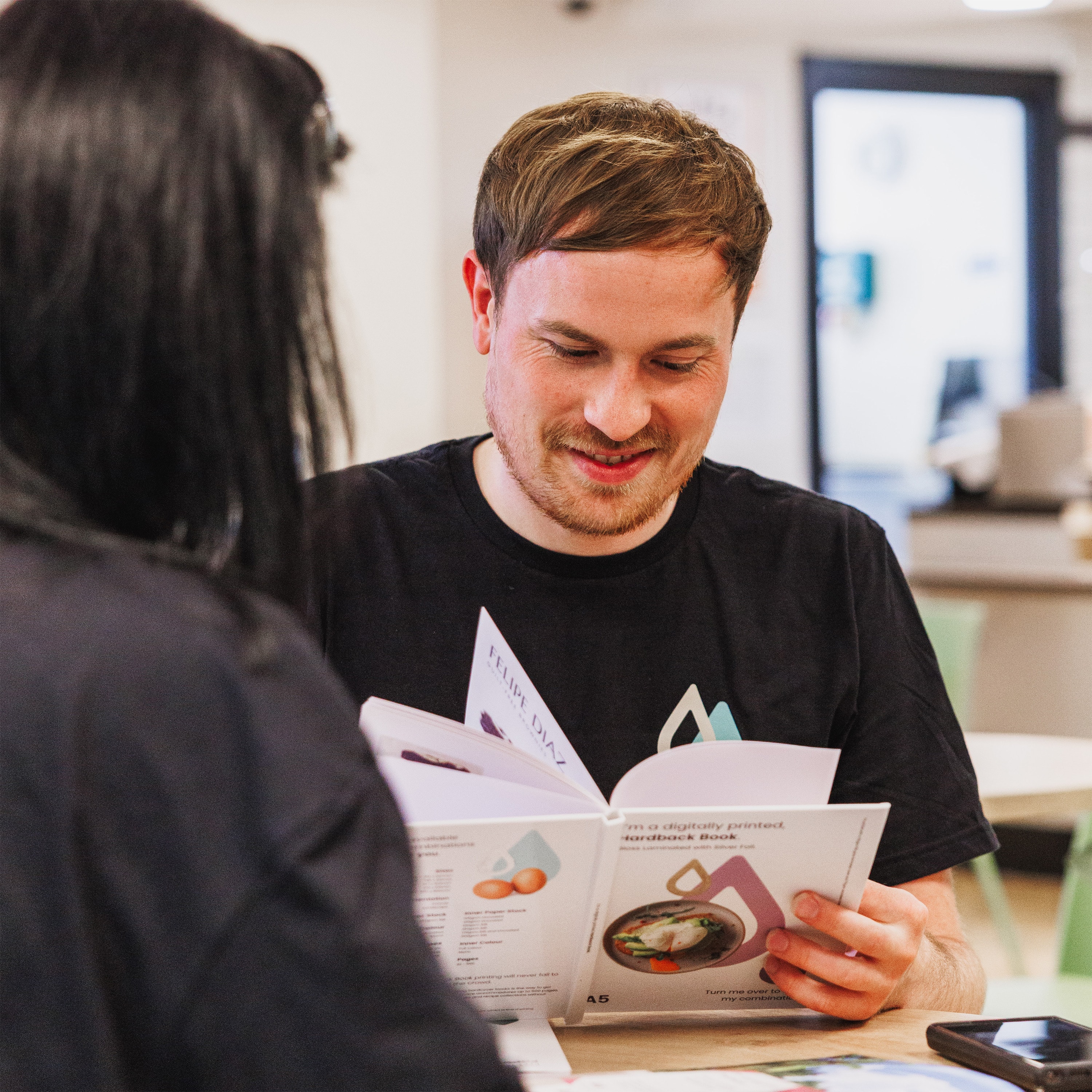 Two people looking at brochures while sitting at a table in a brightly lit room.