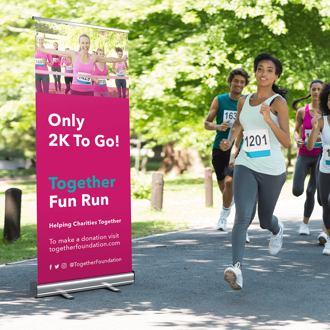 Woman running in a charity race near a "Together Fun Run" roller banner in a park.