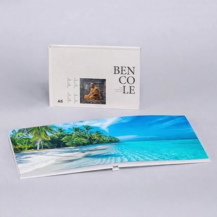 A white photo book with a cover image and an open page showing a tropical beach scene.