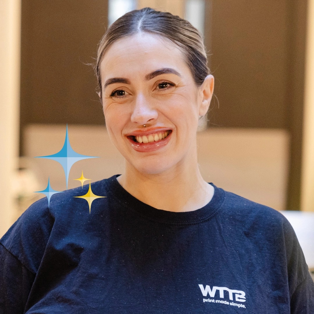 Person smiling, wearing a black shirt with white text in an indoor setting.