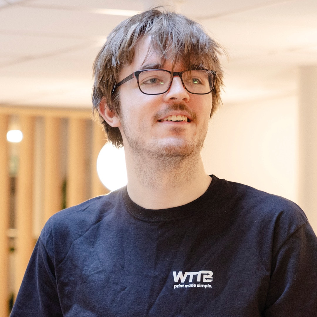 Person with glasses wearing a black WTTB shirt, standing indoors.