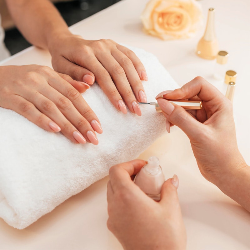 Person receiving a manicure as nail polish is applied to their fingernails on a white towel.