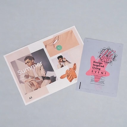 Two printed flyers on a light surface; one advertises "Summer," the other a design event.