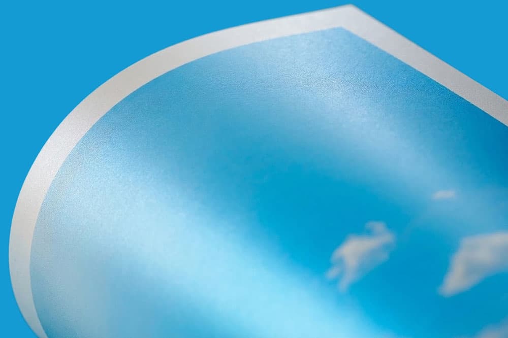 A close-up of a curled sheet of glossy paper with a blue sky and white clouds printed on it.